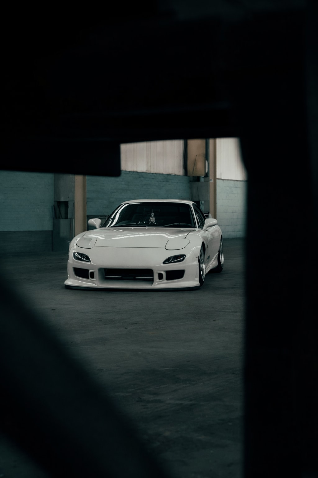 White Mazda RX-7 FD framed through dark foreground inside the warehouse