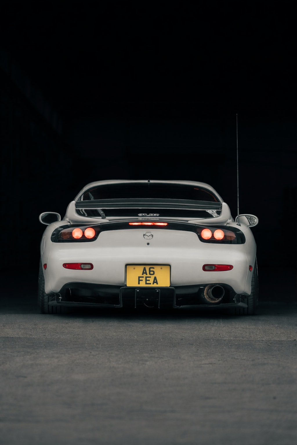 Centered rear portrait of the RX-7 in a dark doorway with tail lights on