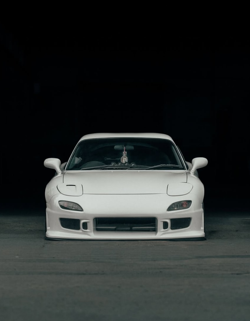 Head-on front view of the white RX-7 against a dark warehouse background