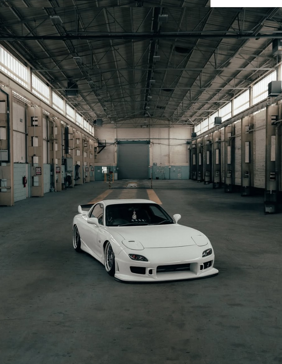 Wide warehouse portrait of a white Mazda RX-7 FD with a low stance